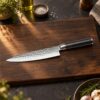 Kōfuku Gyuto Kokkekniv på et bord i mørk eg